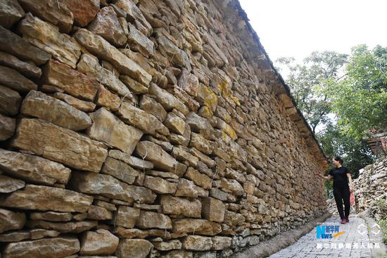 7月30日,河南省宝丰县观音堂林站石板河村,一名游客从石墙边走过.