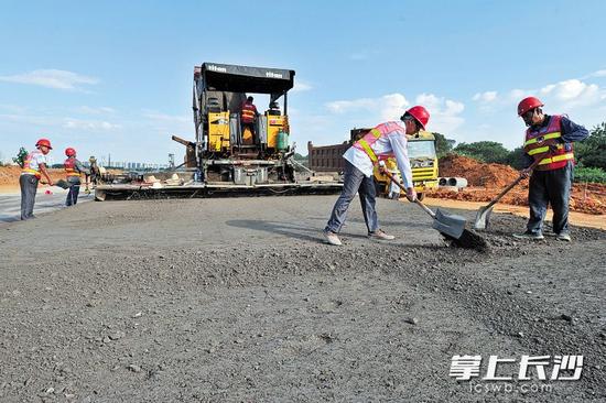 瀟湘北路和銀星路交會處,施工人員使用大型機械攤鋪路面水穩層