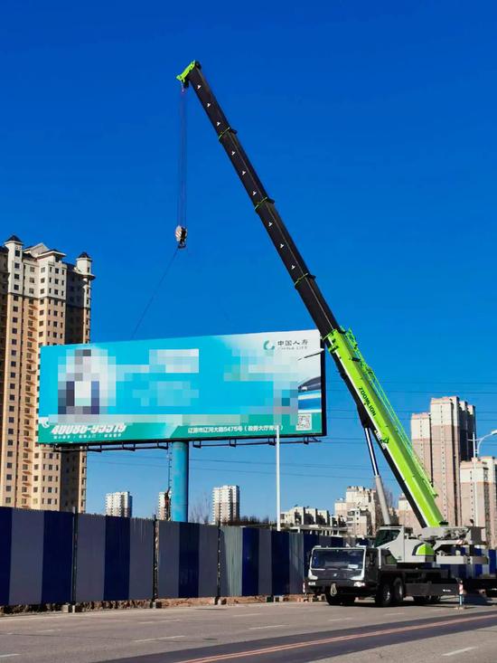名工作人员正在维持秩序,指挥吊车作业人员对三处大型广告架进行固定
