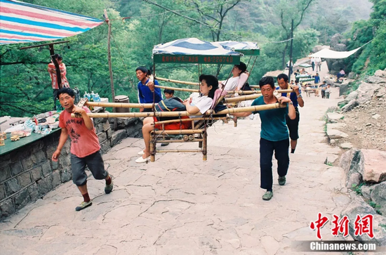 资料图:爬山累得走不动的游客,由挑山工们抬着上山.王德全 摄