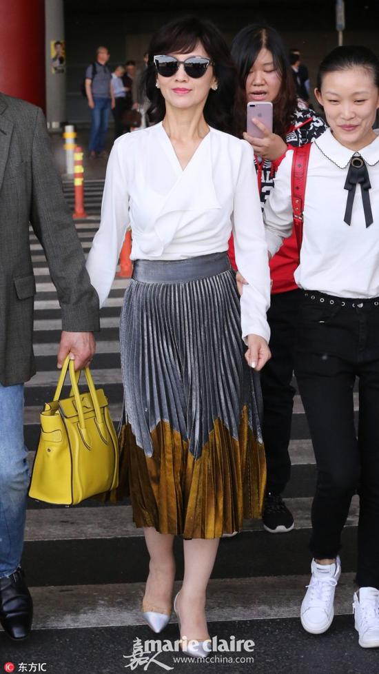 赵雅芝、黄锦燊夫妇现身机场。白色上衣搭配灰色金属光泽拼接百褶裙。