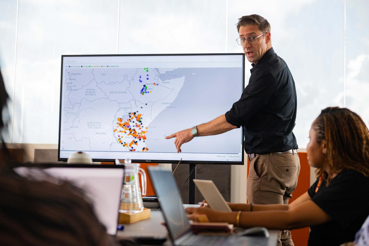 Sanku的聯合創始人費力克斯・布魯克斯-丘奇在坦桑尼亞達累斯薩拿姆的Sanku辦公室帶領團隊開會。會議屏幕上顯示的是Sanku在坦桑尼亞、堅尼亞和埃塞俄比亞合作的所有麵粉廠的數字熱力分佈圖。©Rolex/Peter Ndung’u