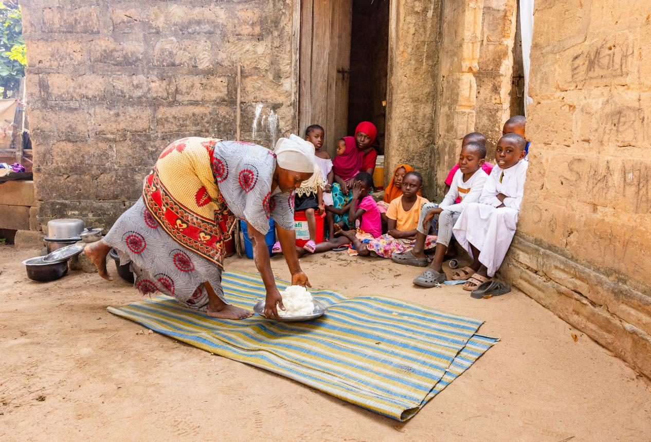 一位婦女在坦桑尼亞維金杜村為一群孩子端上一盤用營養增量麵粉製作的玉米飯（Ugali）。©Rolex/Peter Ndung’u