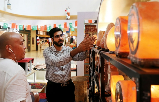 来自巴基斯坦的哈比（右）在位于上海绿地贸易港的商铺内向顾客讲解盐灯的特点和制作过程（9月7日摄）。新华社记者 方喆 摄