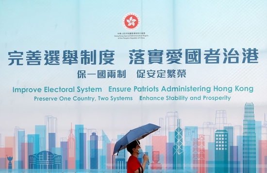 一名香港市民从“完善选举制度 落实爱国者治港”巨幅海报前经过（2021年3月31日摄）。新华社记者 吴晓初 摄