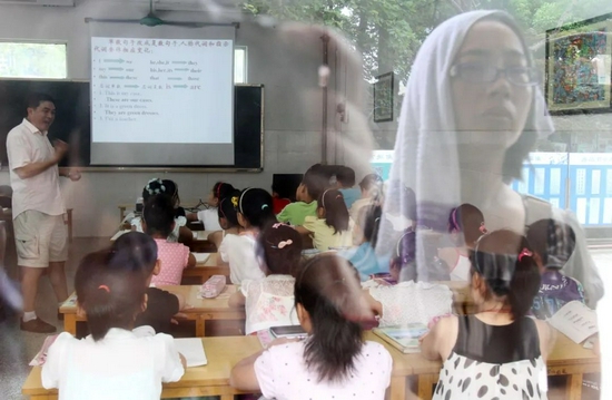 2011年7月7日，江苏省南通市，一名家长头顶毛巾站在教室外隔窗观望正在上“班”的孩子。图/视觉中国 