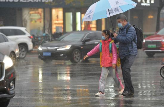  海淀区五道口，一名女生在家长陪同下过马路。绿灯亮起，她伸出手臂示意，转弯车辆也主动停下让行，上演了一幕雨中情。