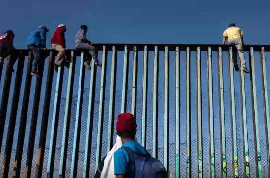 首批抵达美墨边境的移民爬上边境围栏(视频截图)