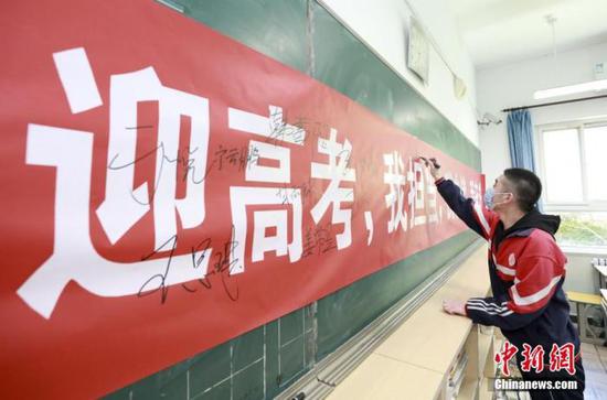 资料图：4月23日，在河北省廊坊市大厂回族自治县回民中学，学生在迎战高考的主题条幅上签名。中新社记者 宋敏涛 摄