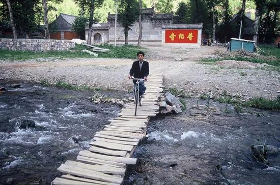 1991年,山西,五台山普化寺外,一名男子在简易的木桥上骑着自行车.