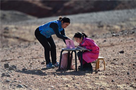 9岁的策耿（右）在家附近的戈壁上网课（4月1日摄）。策耿是内蒙古自治区阿拉善左旗蒙古族学校四年级学生。由于疫情防控，策耿父母长期雇佣的一名外省羊倌没能回到当地，一家人只好回到阿拉善左旗乌力吉苏木温都尔毛道嘎查的牧区家中照看羊群。期间，策耿一边协助父母，一边上网课。新华社记者 刘磊 摄