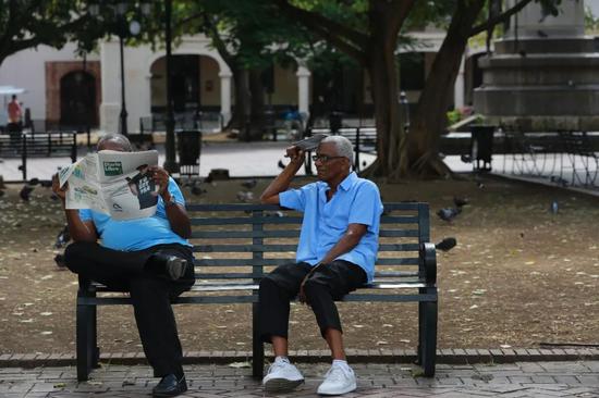 5月2日，在多米尼加首都圣多明各，两位老人在公园长椅上看报休息。新华社记者淡航摄