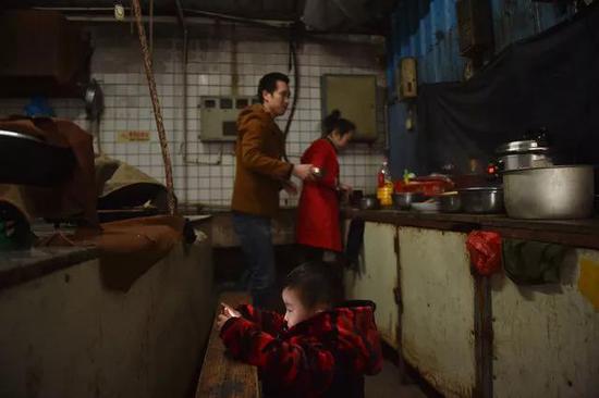黄海龙、黄爱华在工厂宿舍的公共厨房做“团圆饭”，小聪聪在一旁看手机。
