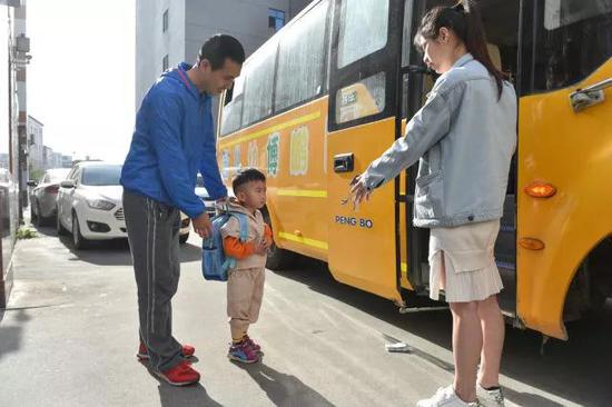 在厂门口，黄海龙（左）将聪聪送上去往幼儿园的校车。
