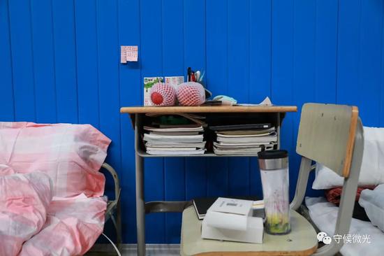  2月21日，武汉市洪山体育馆方舱医院A区内，一名高三学生患者的桌子里放满了书本，墙上贴着的便签是她手写的课程表。晚餐期间每人一份苹果和牛奶，邻床患者将自己那份也送给了她。中青报·中青网见习记者 鲁冲/摄