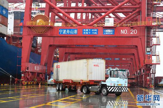 在宁波舟山港梅山岛国际集装箱码头，装有集装箱的卡车从桥吊下驶出（2019年12月19日摄）。新华社记者 黄宗治 摄