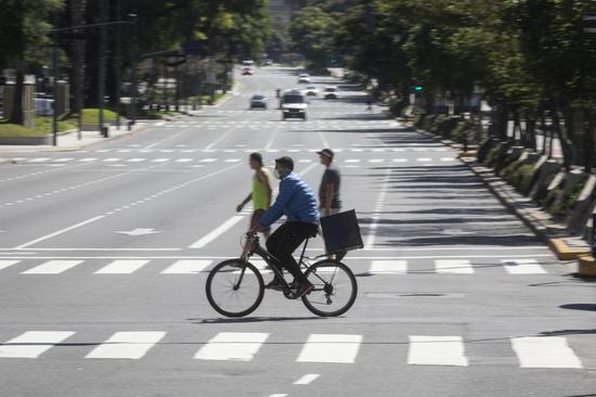  3月20日，在阿根廷布宜诺斯艾利斯，一名戴着口罩的男子骑车经过七月九日大道。新华社发（马丁·萨巴拉摄）