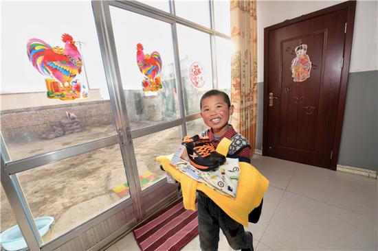 青海互助土族自治县班彦新村的儿童在刚迁入的新居内展示新买的衣服（2017年1月摄）。新华社记者 吴刚 摄