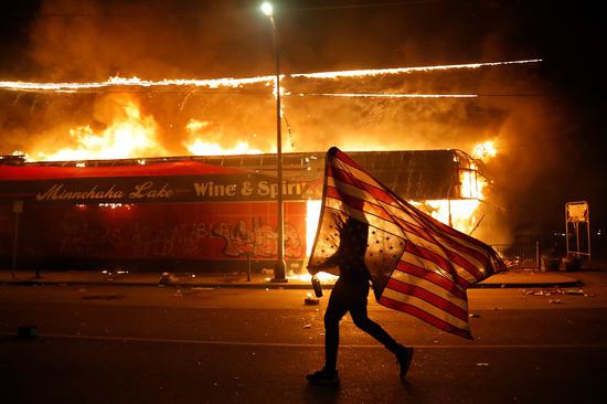 28日，明尼阿波利斯市，一名抗议者倒拿美国国旗奔跑。（美联社）