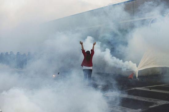 5月30日晚，在美国明尼苏达州明尼阿波利斯市，抗议者在防暴警察施放的催泪瓦斯中与警察对峙。（新华社发，安格斯·亚历山大摄）