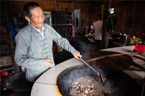在湘西十八洞村，82岁的施成富在自家的农家乐里炒腊肉（6月29日摄）。新华社记者 陈思汗 摄