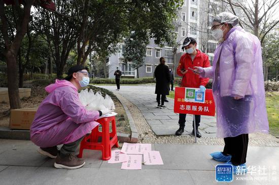 ↑在武汉市江岸区百步亭社区龙庭小区，志愿者张良（左一）向居民核对其团购商品的信息（2月24日摄）。新华社记者 沈伯韩 摄