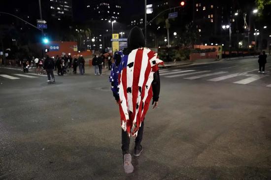 在洛杉矶，一名男子身披被烧毁的美国国旗。