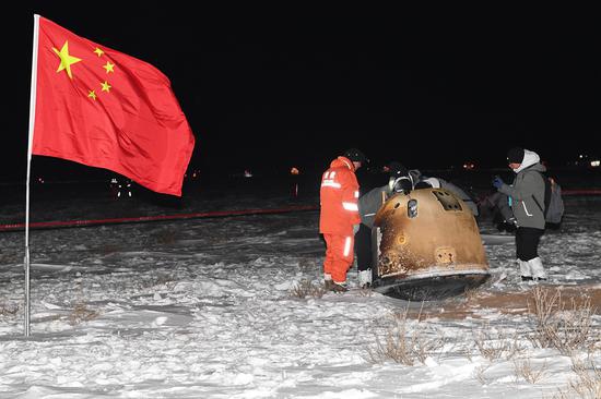 北京时间12月17日1时59分，探月工程嫦娥五号返回器在内蒙古四子王旗预定区域成功着陆，标志着我国首次地外天体采样返回任务圆满完成。五星红旗迎风飘扬，嫦五返回器状态完好，呈直立状态。图为工作人员正在检查返回器状态。摄影/我们的太空创新实践中心 汪江波
