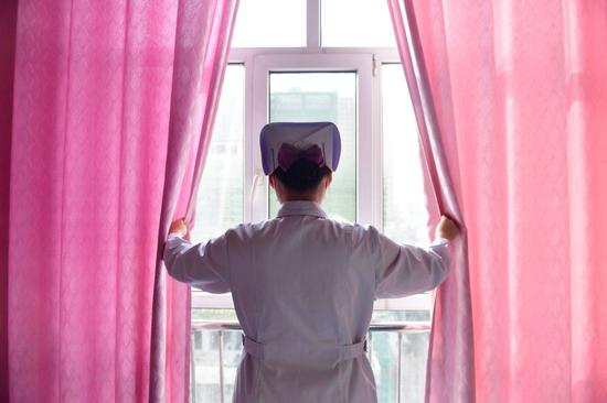 12月16日，海东市第一人民医院内科护士刘海婷在病房内为患者拉开窗帘。