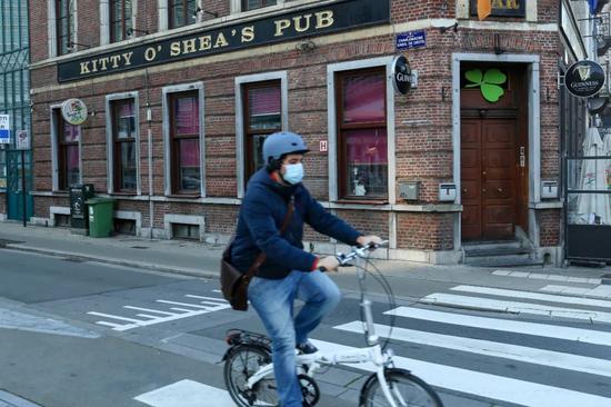 11月5日，在比利时布鲁塞尔，一名戴口罩的男子骑车经过一家关闭的酒吧。张铖摄