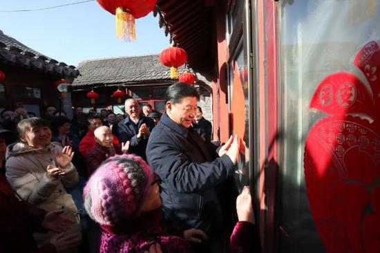  ↑2019年2月1日，习近平在北京前门东区草厂四条胡同32号院，高兴地拿起一幅“福”字，亲自贴到门上，给这里的老街坊们拜年。