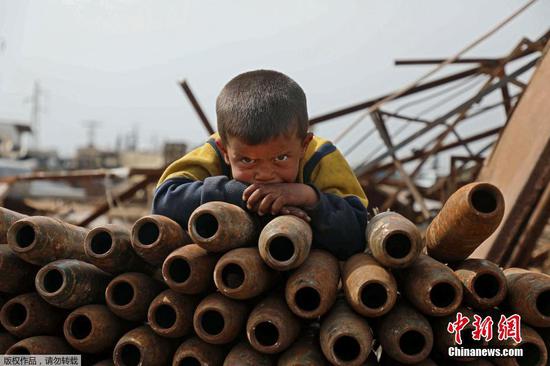 资料图:当地时间2021年3月10日,叙利亚伊德利卜省西北部马雷特米斯林镇郊区的一个金属废料场上,一个小男孩趴在废弃弹壳上。