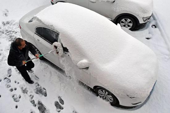  △7日，山东烟台市民在街头清理车上积雪。（图自视觉中国）