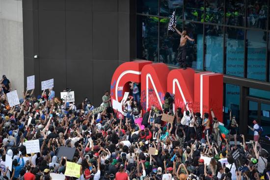 (图说:示威者在CNN总部外观的抗议游走中在徽标上绘画。图源/AP)