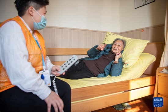2021年12月2日，在重庆市渝北区仙桃街道养老服务中心，陈佩兰老人（右）在护理员陈傲的帮助下体验使用“智能护理床”。新华社记者 唐奕 摄
