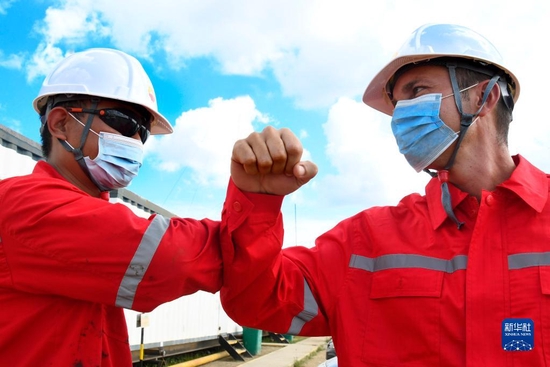 2020年11月27日，中国石油集团长城钻探工程公司古巴项目GW91钻井平台中方员工（左）同古方员工互相致意。新华社发（华金·埃尔南德斯摄）