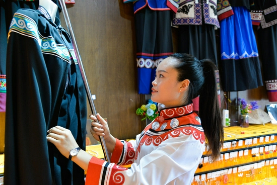 7月15日，在贵州省毕节市大方县奢香古镇，彝族姑娘龙恩碧在自己的彝族服饰和手工艺品店整理商品。新华社记者 徐钦 摄