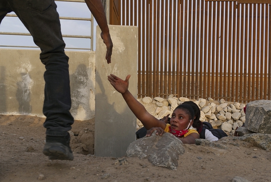 一名移民从边境墙的一个缺口伸出手寻求帮助。
