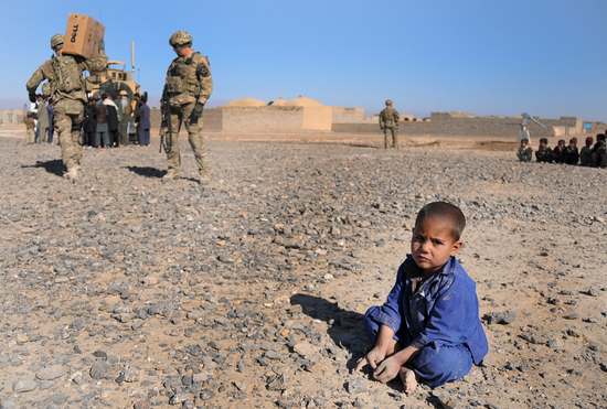 ▲2013年2月，阿富汗法拉赫省一名小男孩在尘土中玩耍，他身边就是荷枪实弹的美国大兵。
