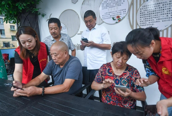  2021年8月，在杭州市临安区锦南街道锦溪社区，志愿者向老年人讲解手机软件的使用方法（新华社记者徐昱 摄）