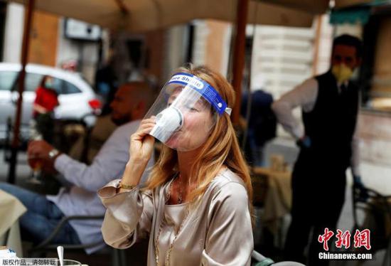 意大利政府依照计划5月18日开始松绑禁令，重启社会生产经营活动，并开放相关旅游、游乐等公众设施。图为戴面罩的女士在罗马街头喝咖啡。