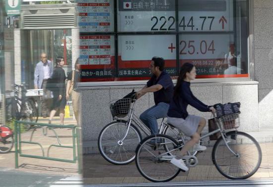 资料图：在日本东京，市民骑车经过显示股市信息的电子显示屏。 （新华社）