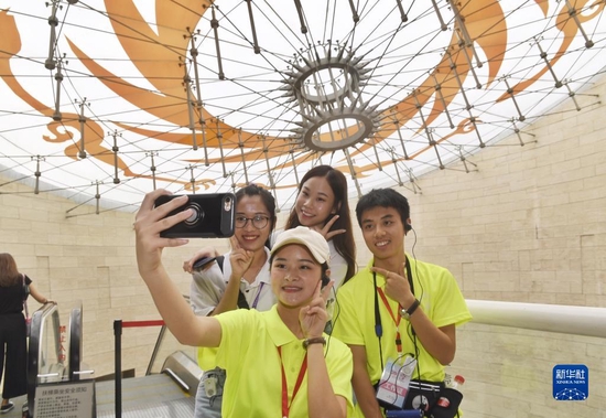 参加交流活动的香港青年（后排）在四川金沙遗址博物馆陈列馆有“太阳神鸟”图案的房顶前与志愿者（前排）合影留念（2019年8月25日摄）。新华社记者刘坤摄
