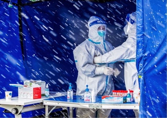 2021年12月25日，咸阳市华府御园小区核酸检测现场，医护人员在风雪中相互取暖。马晓萍 摄
