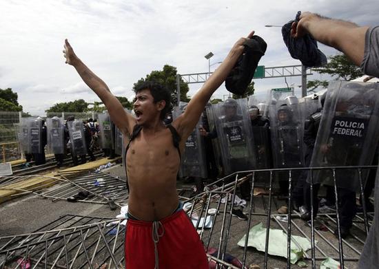 一名年轻移民站在墨西哥警察面前，大声呼喊，让大家冷静（美联社）