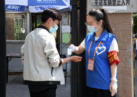 在北京市海淀区中关村街道白塔庵社区出入口，社区志愿者王玥（右）为居民测量体温（6月16日摄）。新华社记者 任超 摄