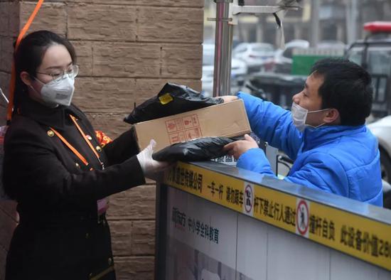 疫情期间，一位志愿者（左）接过快递员送来的社区居民的快递 任超/摄