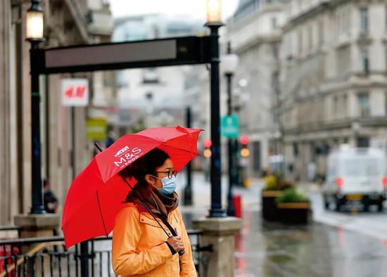  12月21日，一名戴着口罩的女子打伞站在英国伦敦街头。韩岩摄