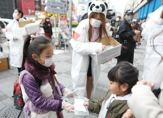 2月29日,在日本东京的池袋站前,在日华侨华人志愿者团体“口罩熊猫行动小组”向当地民众免费发放口罩,一名小志愿者(左)将儿童用口罩送给日本小朋友。新华社记者 杜潇逸 摄