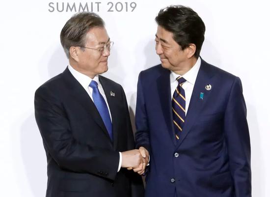 6月28日,日本首相安倍晋三迎接韩国总统文在寅抵达会场,两人握手。